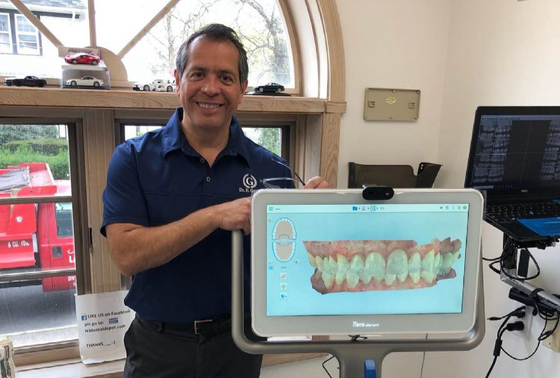 A man standing next to a dental model with a computer displaying an X-ray image behind him.